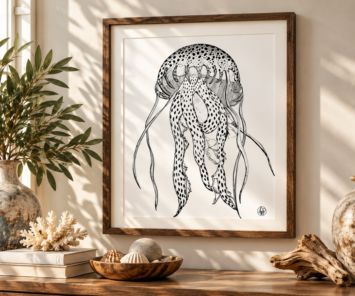 A framed black and white line art print of a jellyfish hanging on a warm beige wall above a wooden console table styled with seashells, driftwood, and a potted plant.