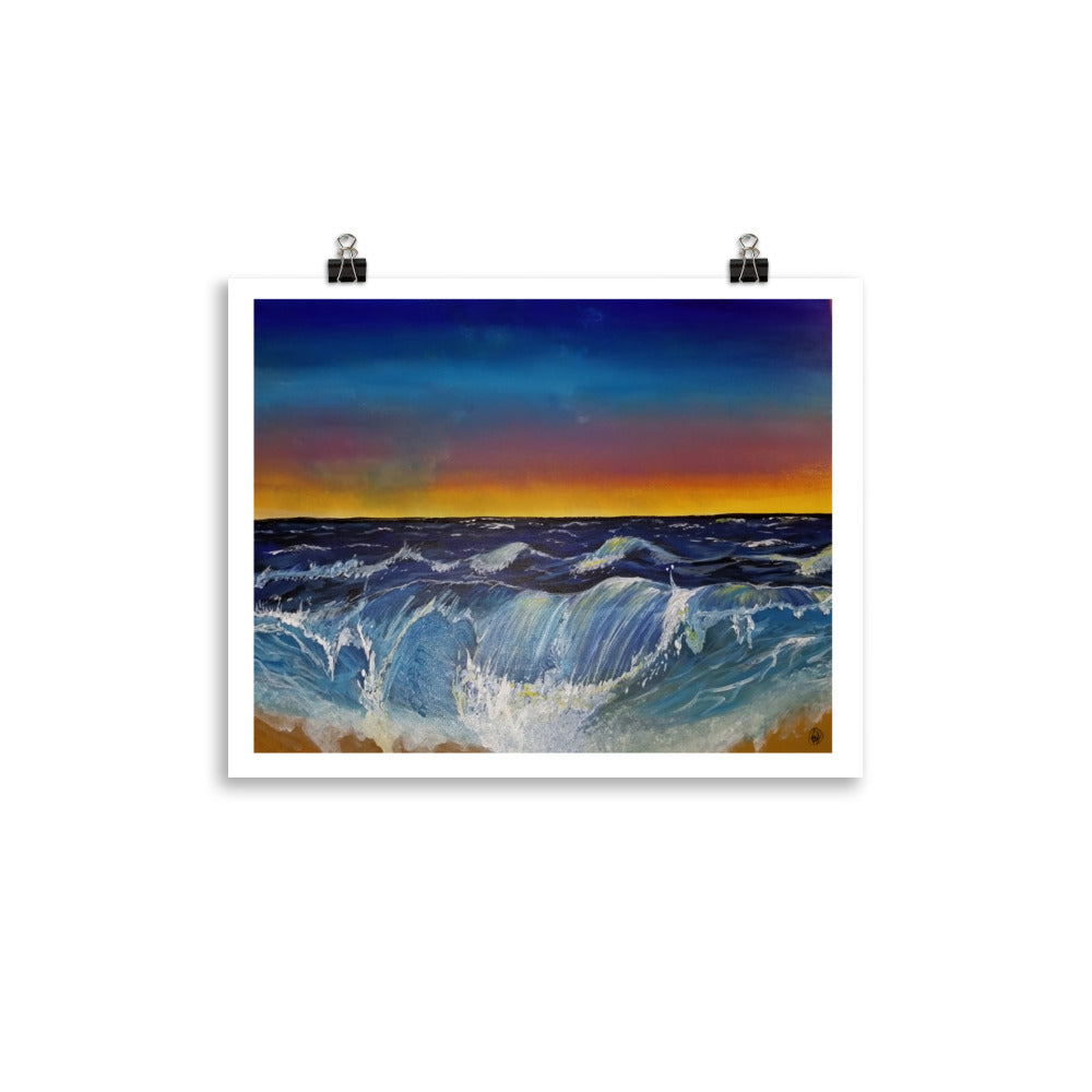 A square art print depicting a dramatic ocean scene with blue and white waves under a dark blue and orange sunset sky, hung on a white wall with two black binder clips.