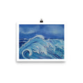 A square art print depicting a powerful blue ocean wave with white foam under a deep blue sky, held by a black binder clip against a clean white background.